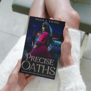 Book - Precise Oaths - in the hands of a woman wearing a white sweater dress.