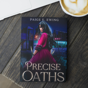 Precise Oaths paperback on table with coffee and a laptop